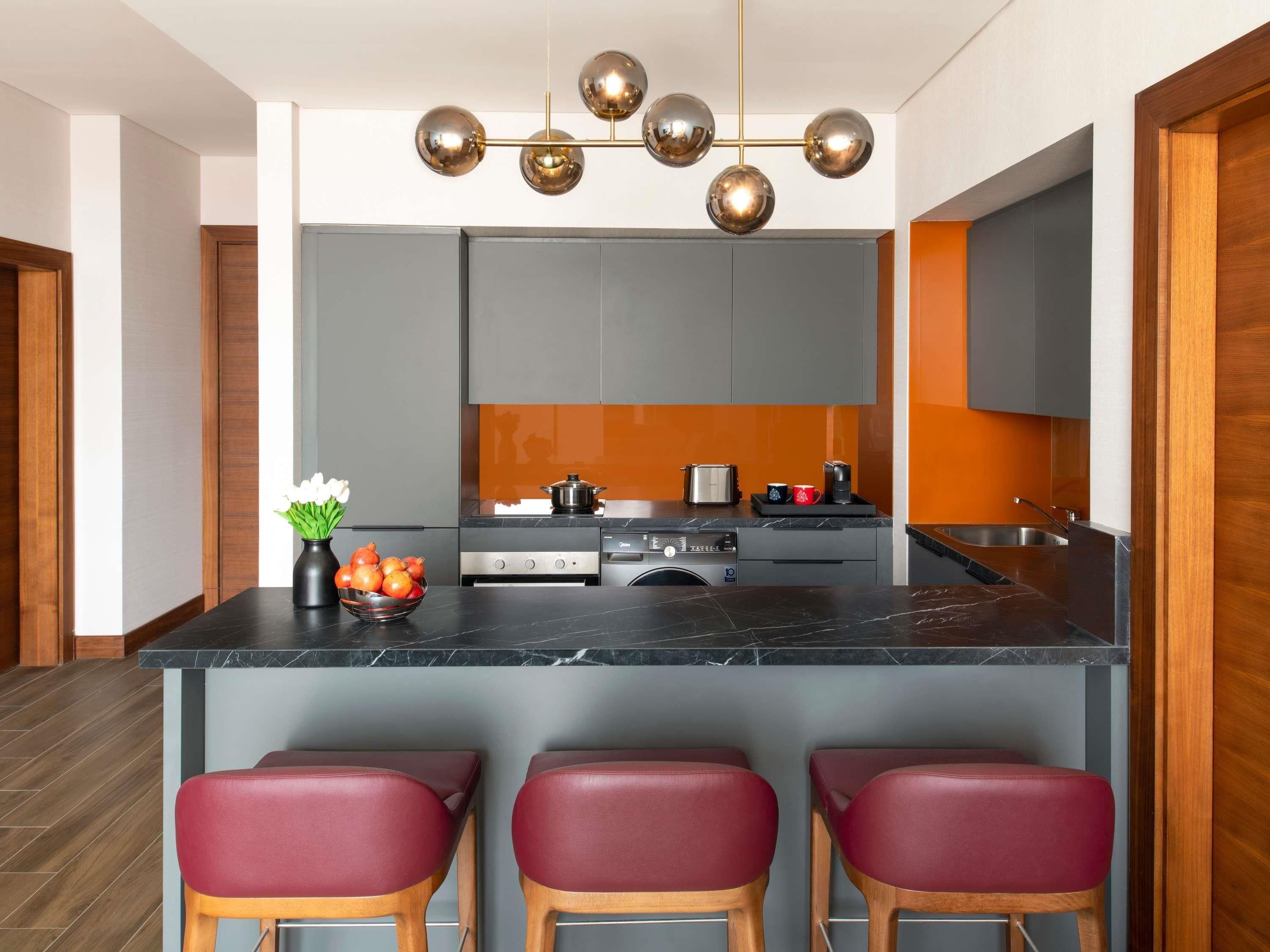 A modern kitchen with grey cabinets, a central island with stools, a coffee machine, and a pot on the stove.