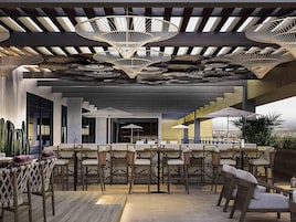 Un espace bar extérieur avec des fauteuils en osier, un plafond à motifs et une vue sur la ville.