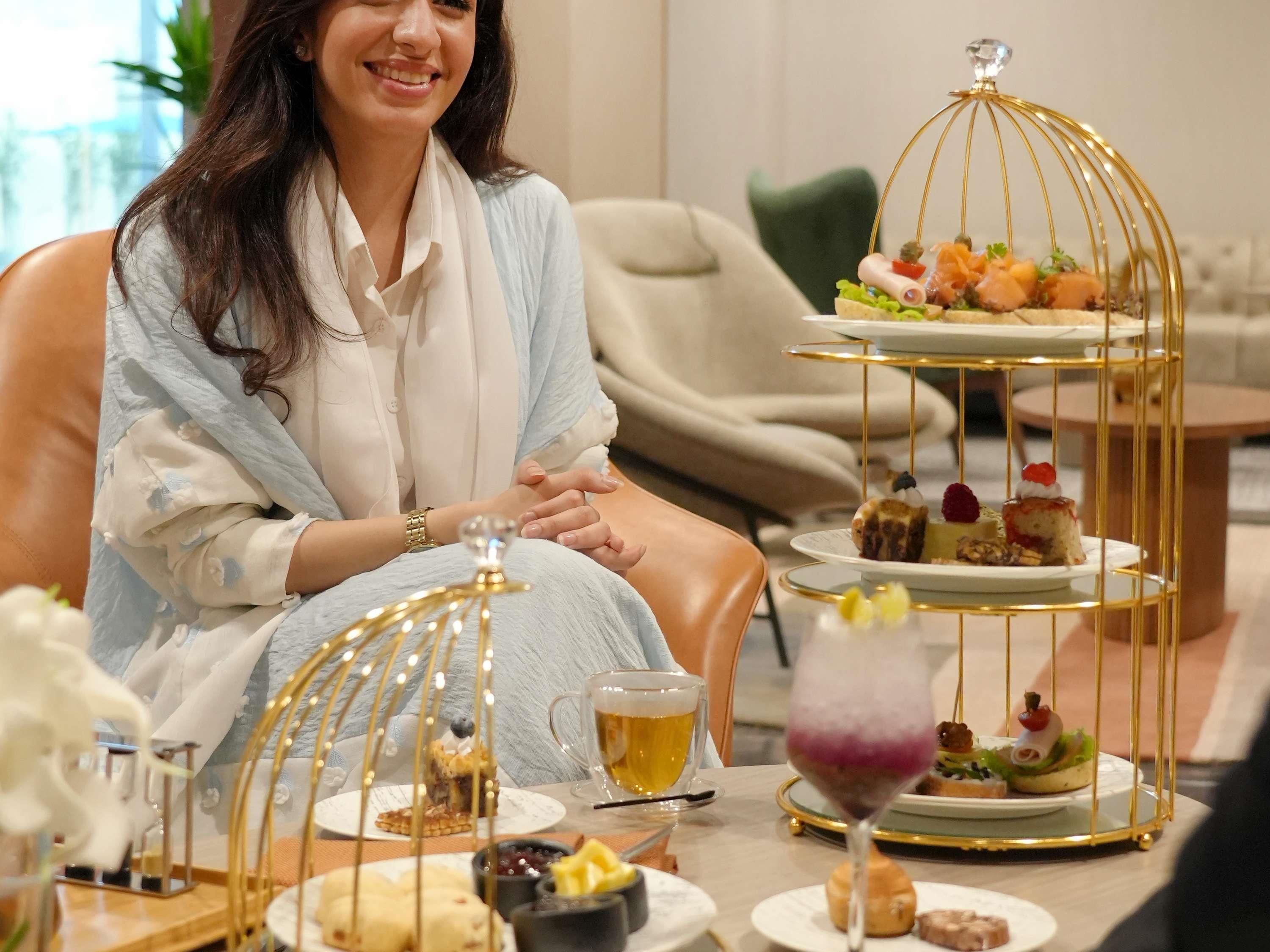 A person seated at a table with a three-tiered dessert stand, a glass of beer, and various small dishes.