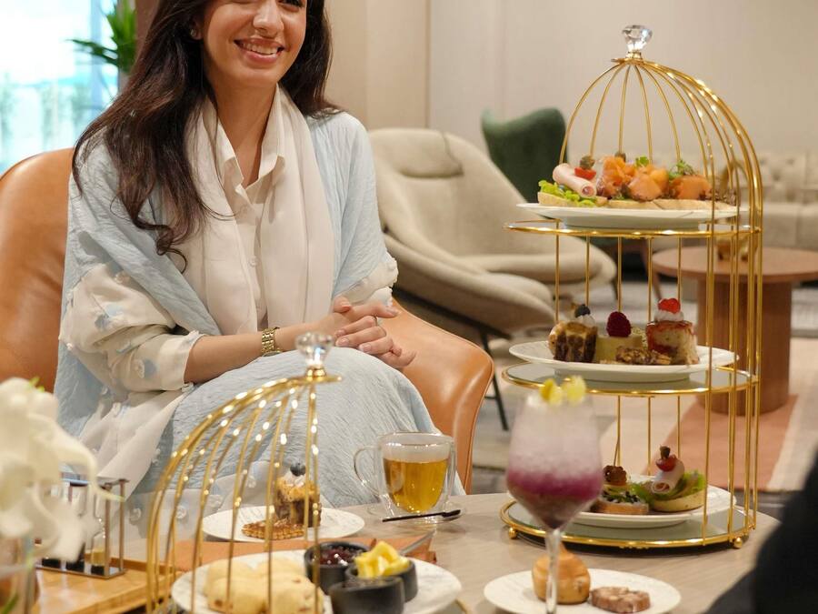 A person seated at a table with a three-tiered dessert stand, a glass of beer, and various small dishes.
