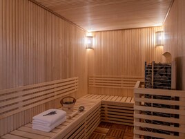 A sauna with wooden benches, a towel, a basin, and a rock storage rack.