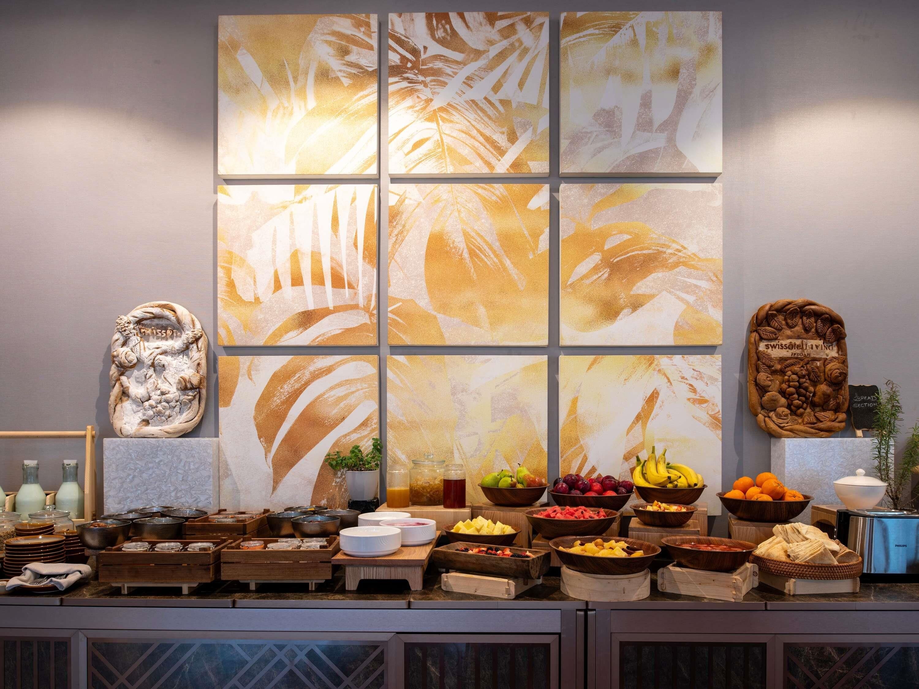 Un bufé de desayuno con diversos alimentos y un cuadro abstracto grande en la pared.