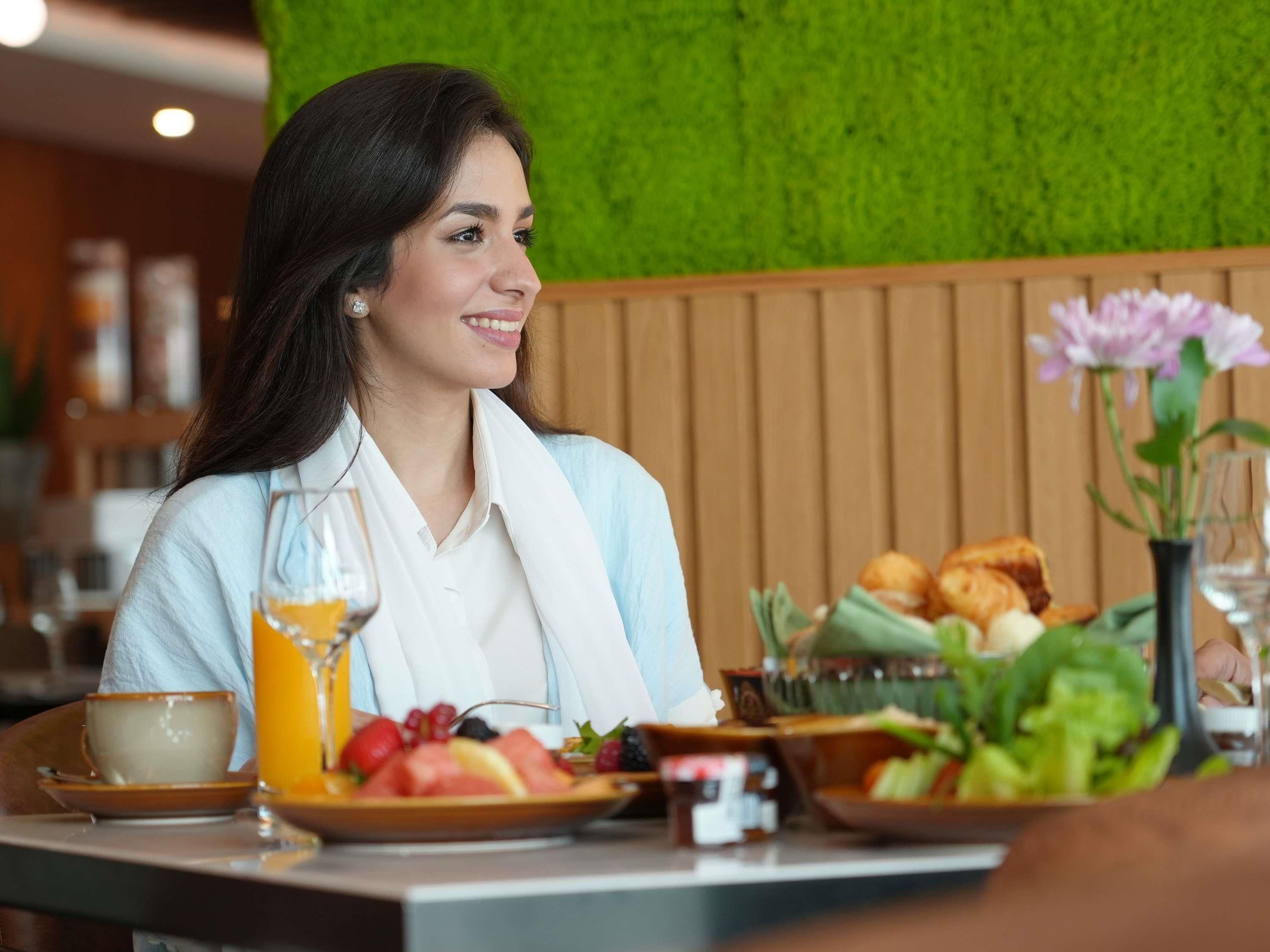 Una persona sentada a la mesa con alimentos para el desayuno, como tostadas, fruta y una bebida.