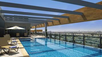 Una piscina infinita en la azotea con sillones de descanso y sombrillas, rodeada por una pérgola de madera y vistas a la ciudad.