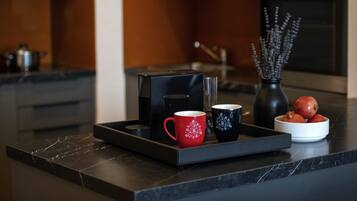 Una cocina moderna con encimera negra, una cafetera, dos tazas, un florero con flores y un cuenco de fruta.