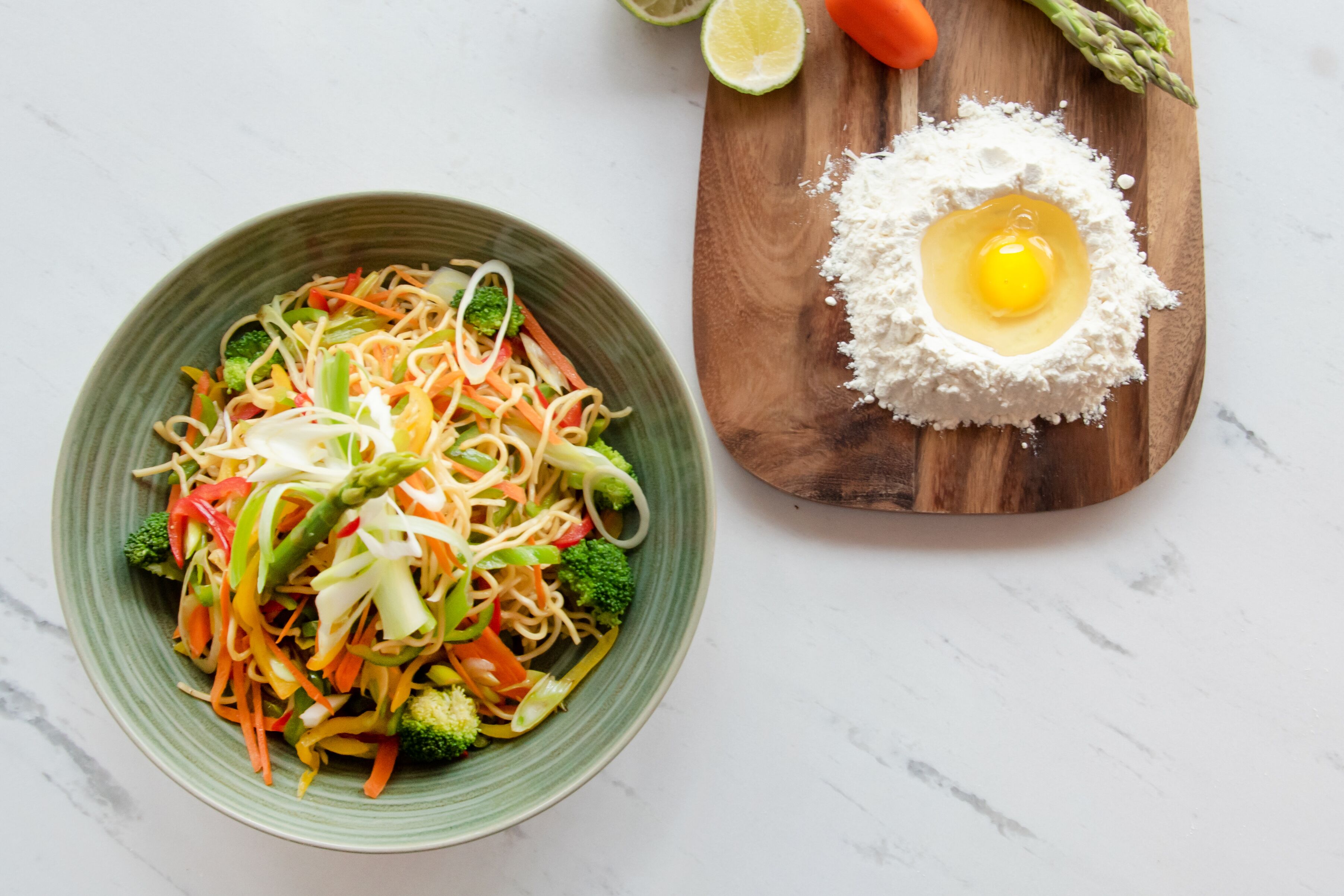 A plate of vegetable stir-fry with noodles and a wooden board with a raw egg yolk.