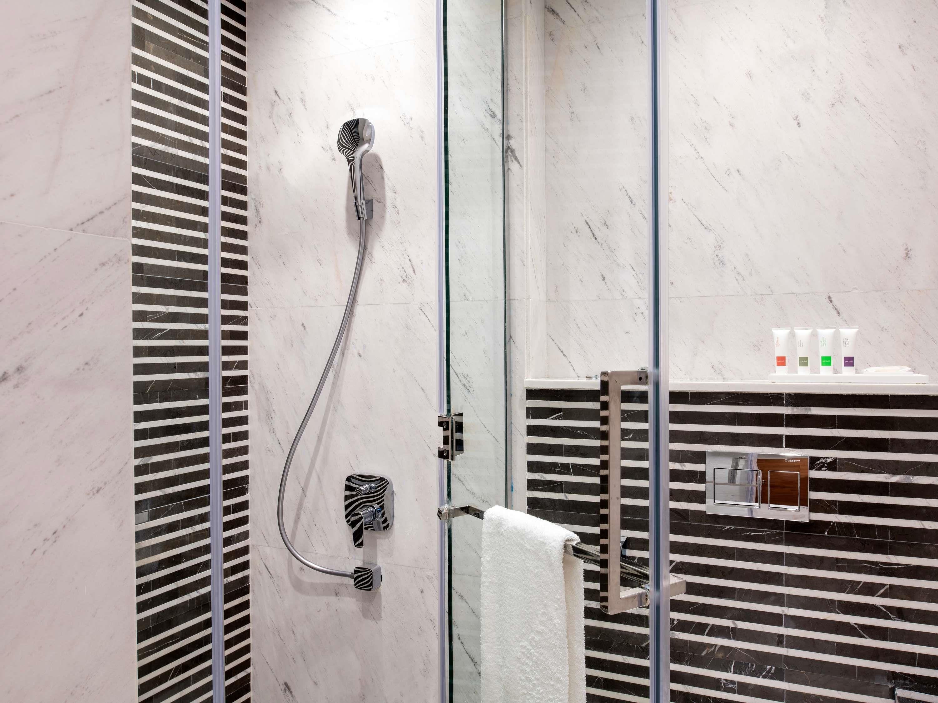 Et badeværelse med brusebad, håndklædestang og toiletartikler på en hylde.