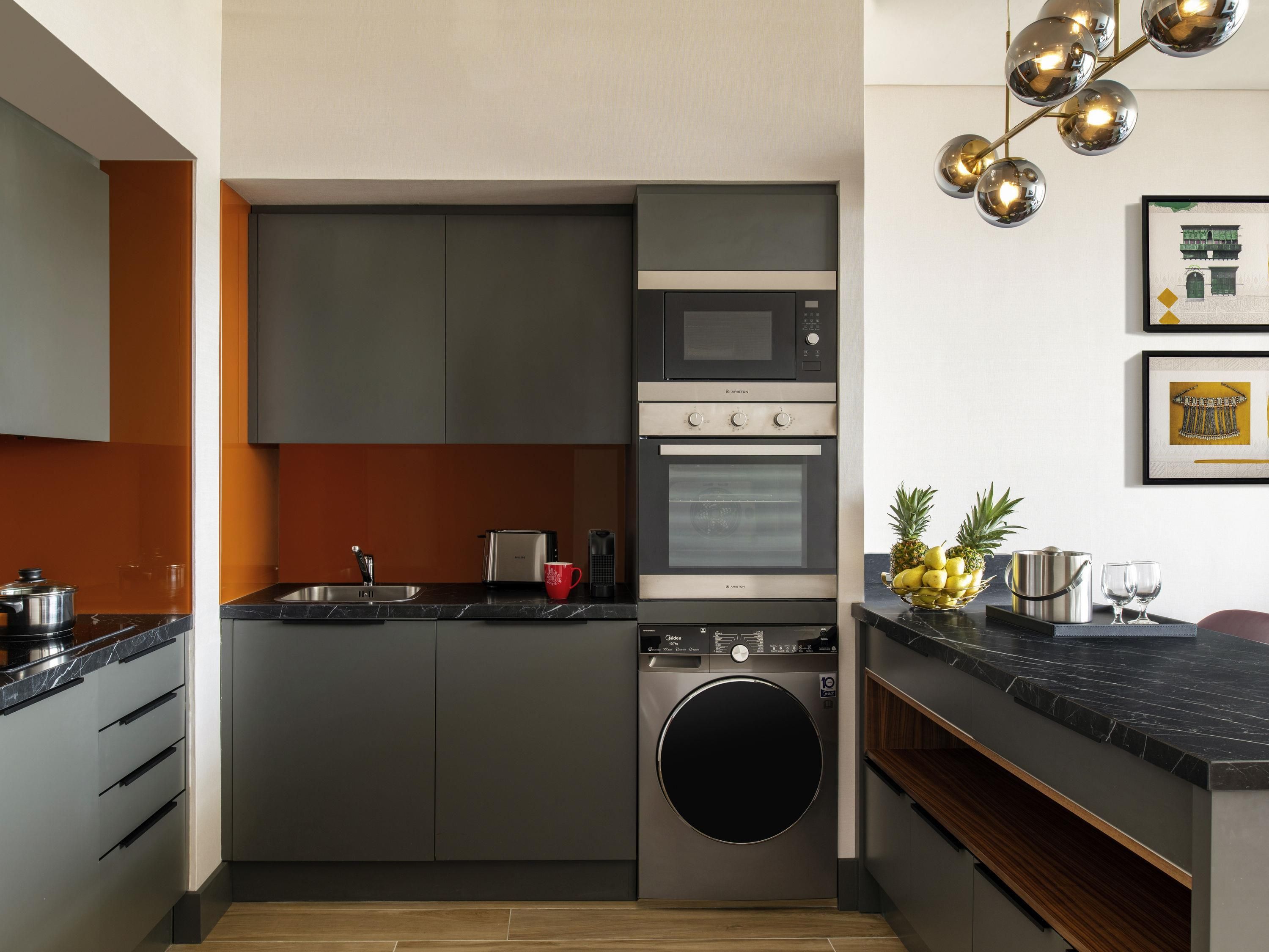 A modern kitchen with a built-in oven, microwave, and dishwasher. There is a sink with a faucet, a toaster, and a red mug on the counter. A washing machine is visible in the corner.