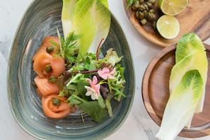 A plate of food with salmon, greens, and capers. - Swissotel Living Jeddah (Jeddah)