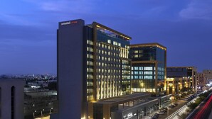 Un hotel moderno con diversi piani, un'area di parcheggio e vista sullo skyline al crepuscolo.