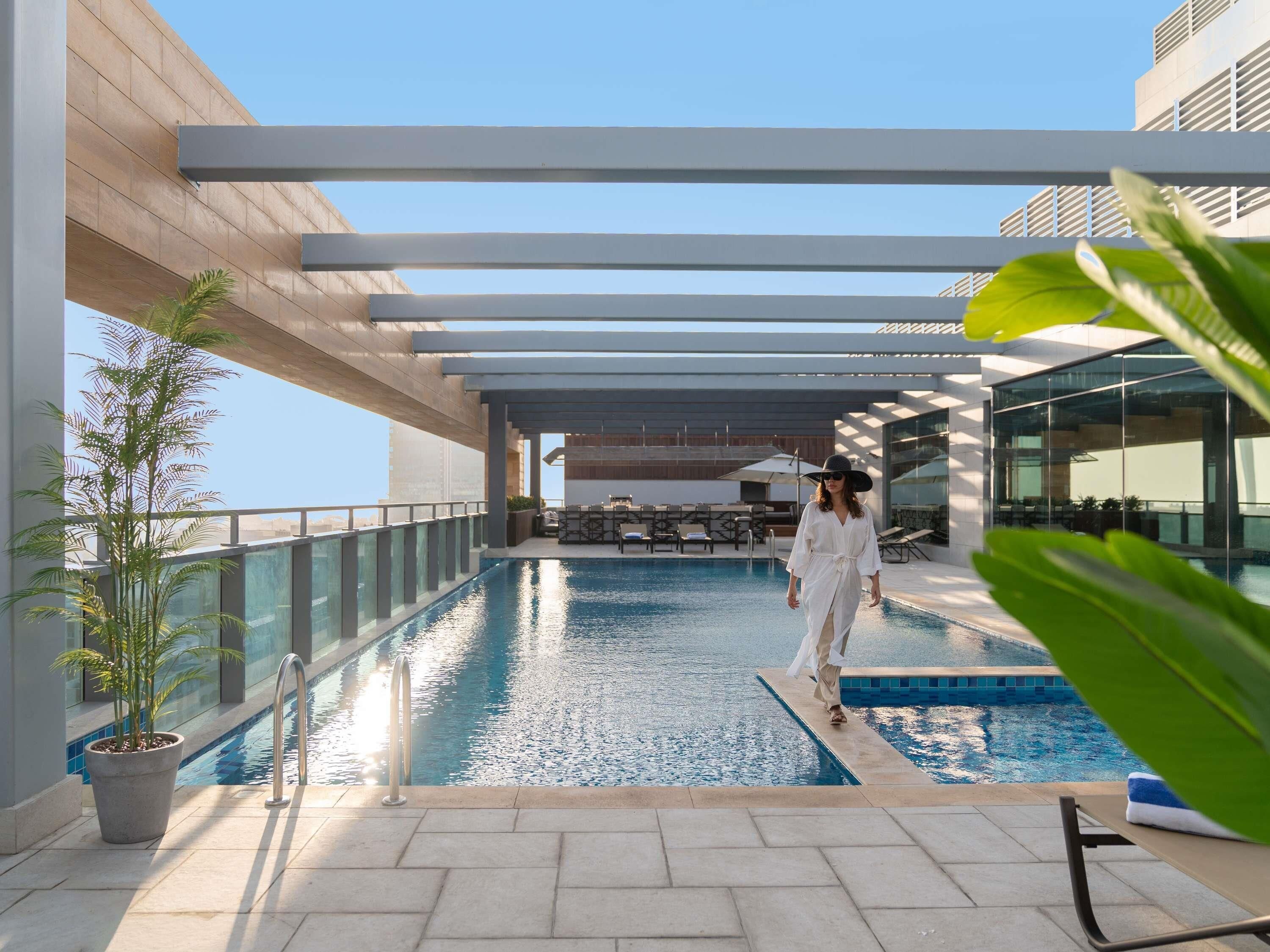 A poolside area with a person walking, a pool, and outdoor furniture.