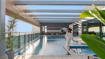 Zona de piscina con una persona caminando, una piscina y mobiliario exterior.