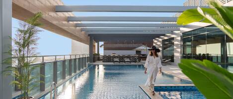 A poolside area with a person walking, a pool, and outdoor furniture.