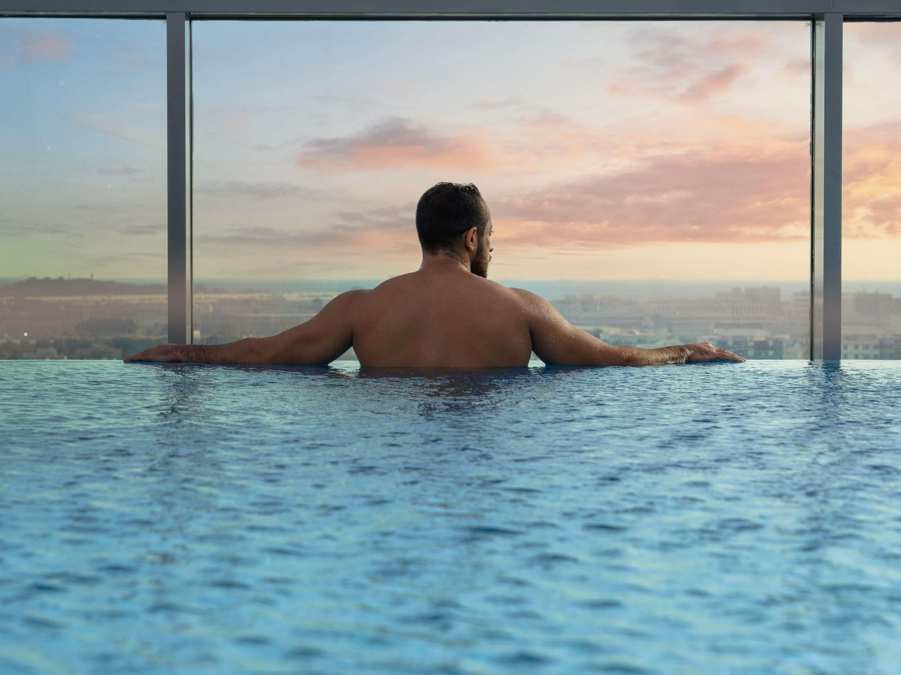Una persona en una piscina interior amplia con vistas a un paisaje urbano a través de grandes ventanales.