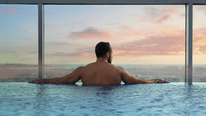 Una persona in una grande piscina al coperto con vista su un panorama urbano attraverso ampie finestre.