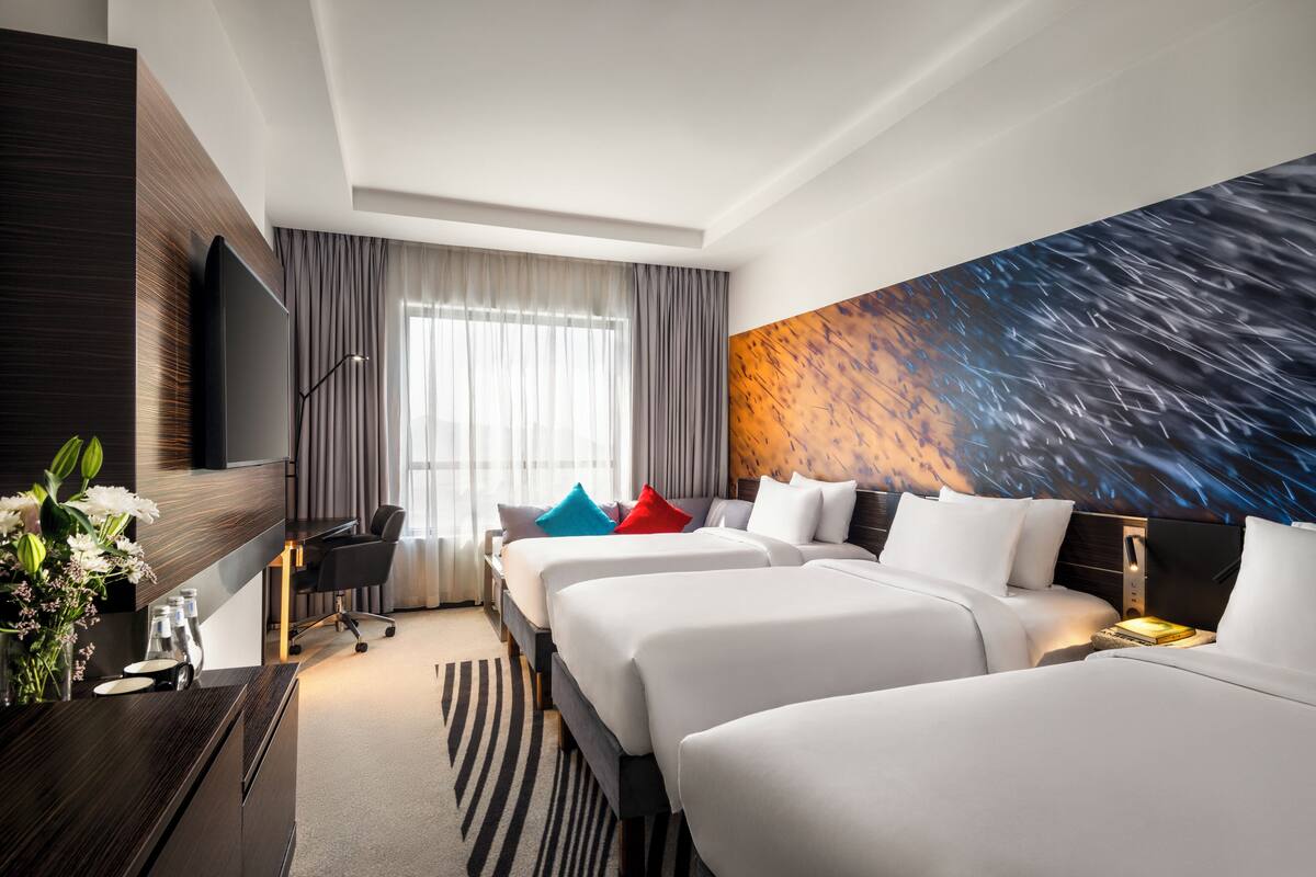 A hotel room with two beds, a desk, a TV, and a large wall mural.