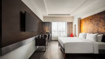 Une chambre d’hôtel moderne dotée d’un grand lit, d’un téléviseur à écran plat fixé au mur, d’un bureau avec une chaise et d’une fenêtre avec des rideaux.