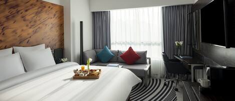 Una habitación de hotel moderna con una cama grande, un escritorio, un televisor de pantalla plana y un ventanal con cortinas.