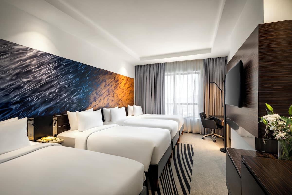 A hotel room with three beds, a large wall mural, a flat-screen TV, and a desk with a chair.