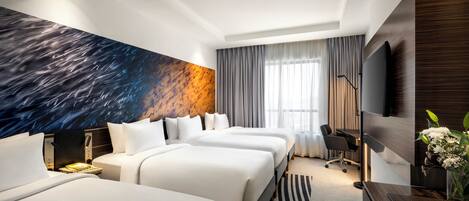 Habitación de hotel con tres camas, un mural grande en la pared, un televisor de pantalla plana y un escritorio con una silla.