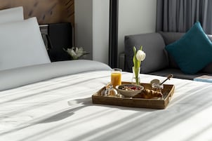 Una bandeja de desayuno bien dispuesta sobre la cama, con un croissant, un tazón de cereal y un vaso de jugo de naranja.