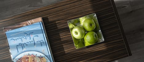 A book and a glass container with green apples on a wooden table.