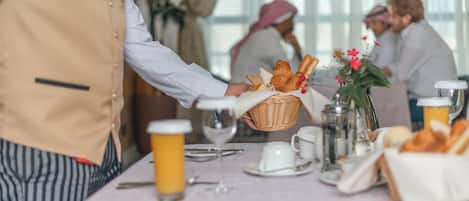 A breakfast setting with a table set for four, including bread, pastries, and a vase with flowers.