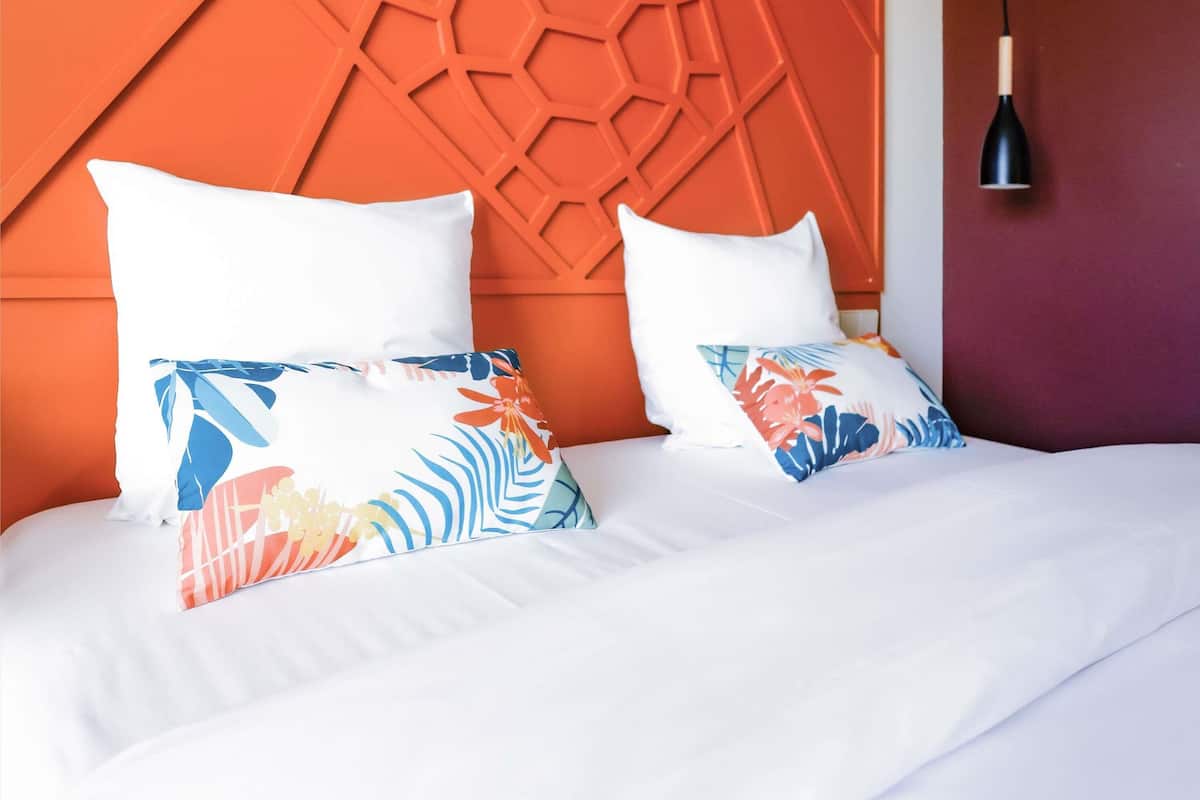A bed with white bedding and two decorative pillows with tropical patterns.