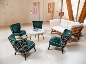 Une pièce avec un canapé blanc, deux fauteuils verts, une table ronde et une chaise en bois.