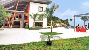 A modern building with a flat roof, large windows, and a covered outdoor seating area with red chairs. - Ibis Styles Mayotte Aeroport (Pamandzi)