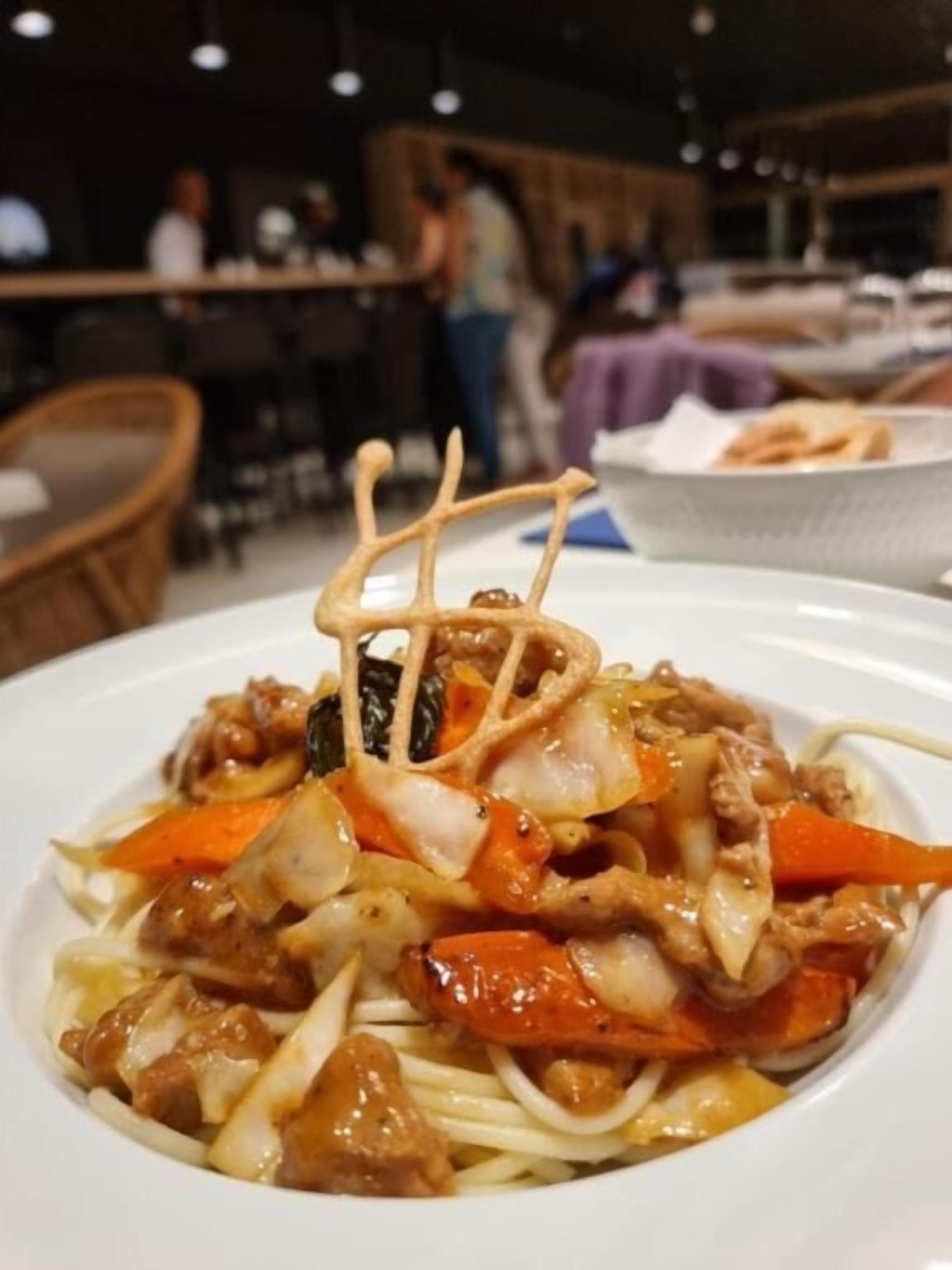 Un ambiente de restaurante con un plato de fideos y verduras, una silla de madera y una mesa de comedor.