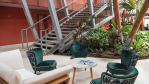 A seating area with green upholstered chairs and a wooden sofa, a small round table, and a staircase in the background. - Ibis Styles Mayotte Aeroport (Pamandzi)