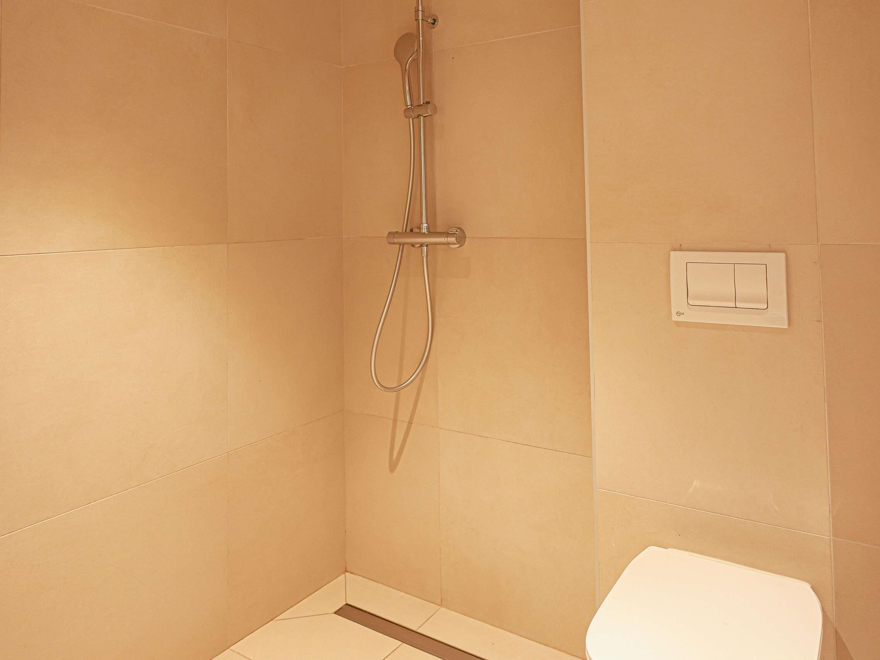 A small, tiled bathroom with a shower, toilet, and a light switch on the wall.
