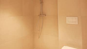 Un baño pequeño con azulejos, ducha, inodoro y un interruptor de luz en la pared.