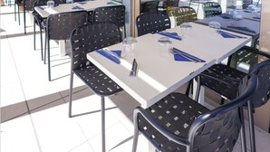 A restaurant with outdoor seating, tables, and chairs, overlooking a pool and mountains. - Ibis Styles Mayotte Aeroport (Pamandzi)