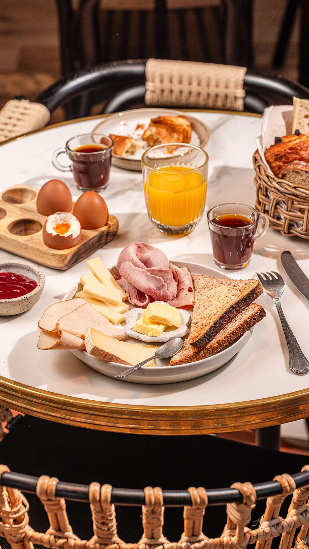 Una mesa de desayuno con huevos, jamón, queso, tostadas y bebidas.