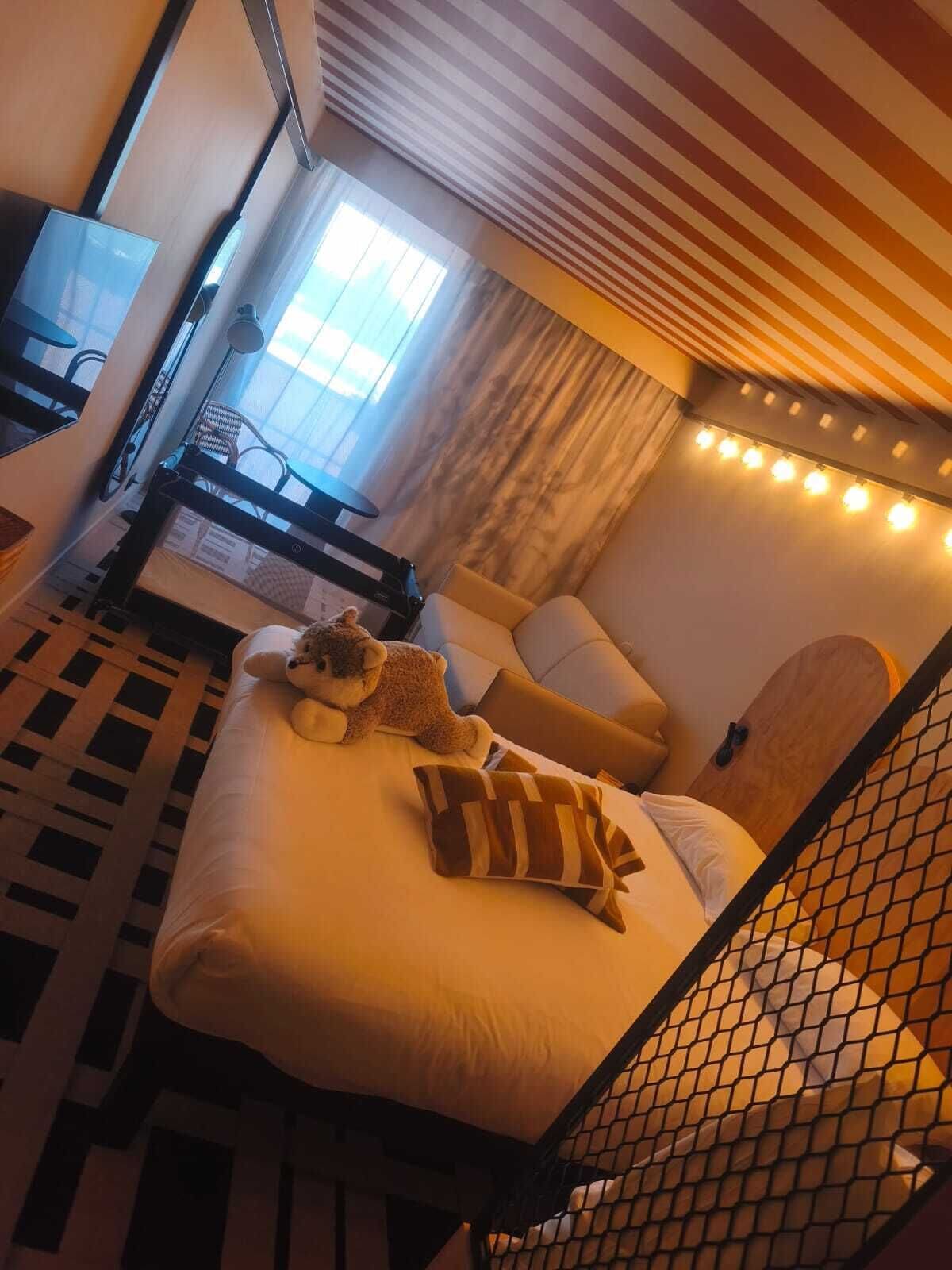 Quarto de hotel com cama, cadeira, escrivaninha e janela.