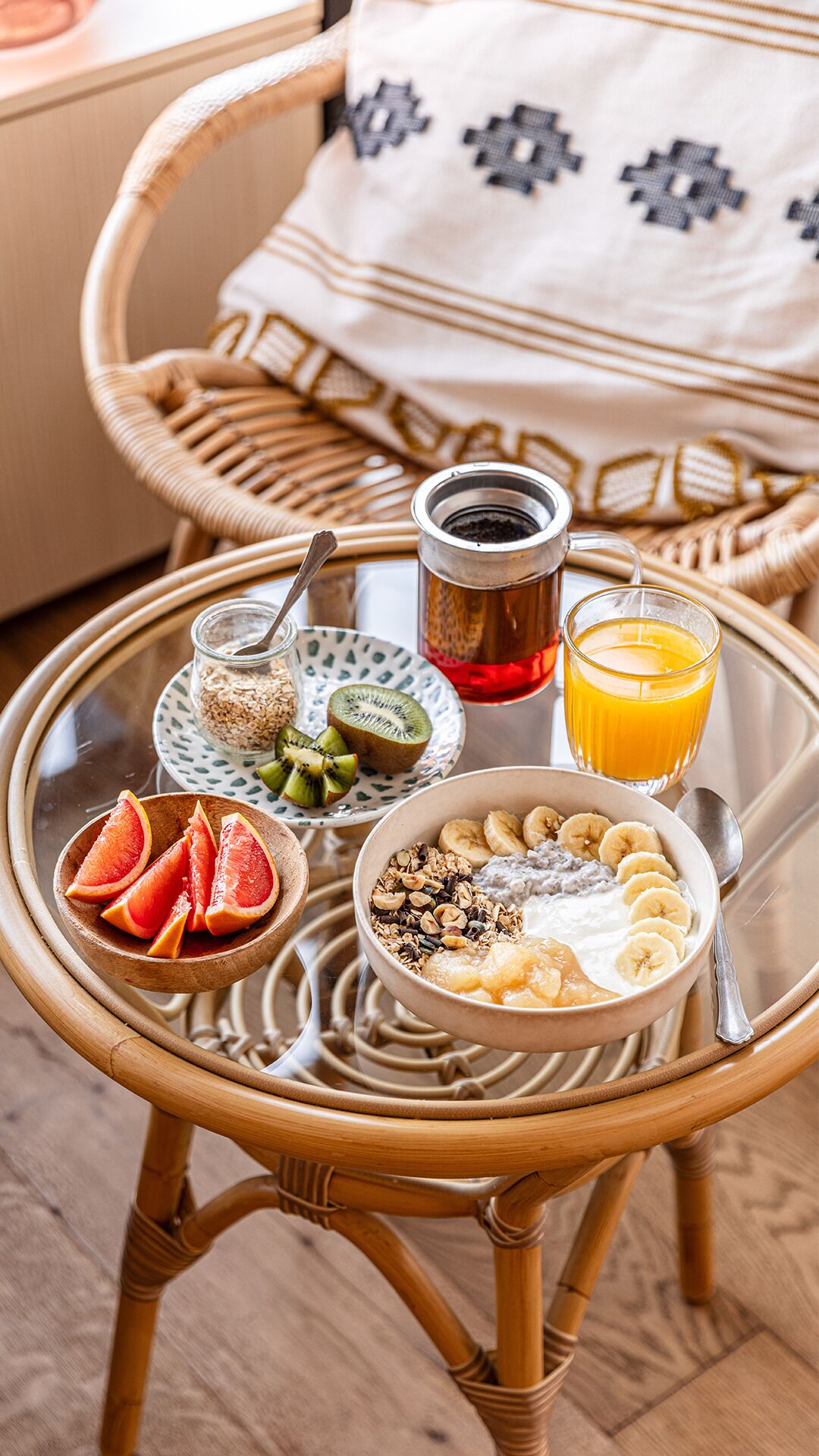 Una mesa de desayuno con diversos alimentos, un vaso de jugo de naranja y una taza de té.