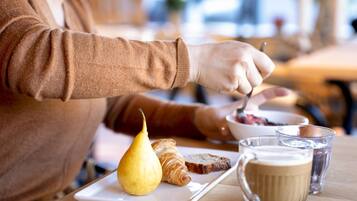 A person eating breakfast with croissants, a pear, and coffee on a wooden table.