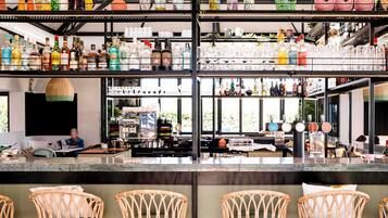 A bar with multiple shelves of bottles and glasses, a coffee machine, and wicker chairs.