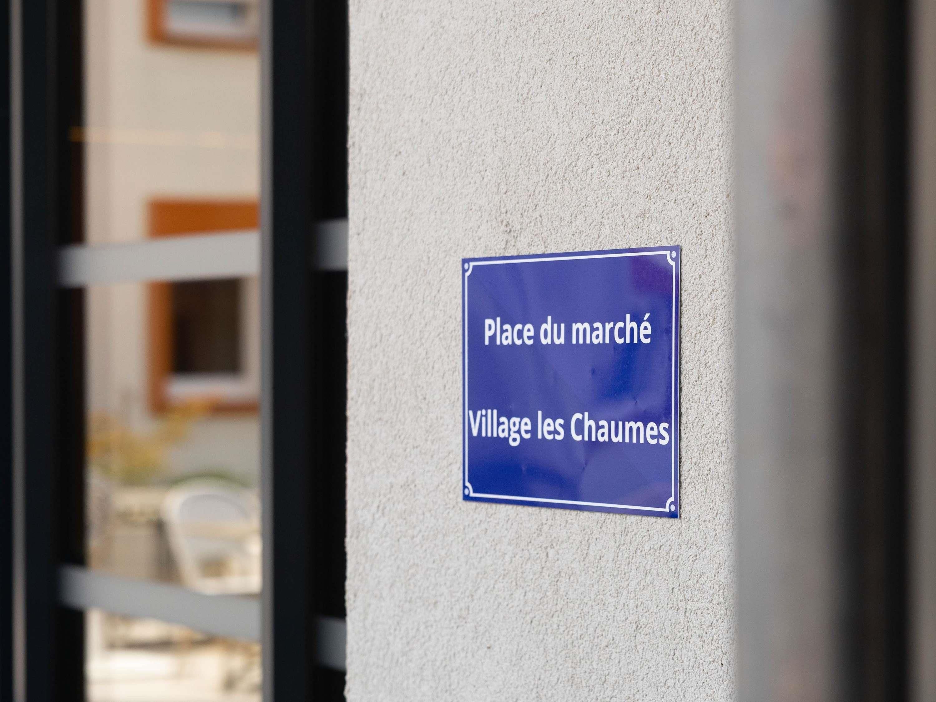 Un cartello su una parete indica 'Place du marché Village les Chaumes'.