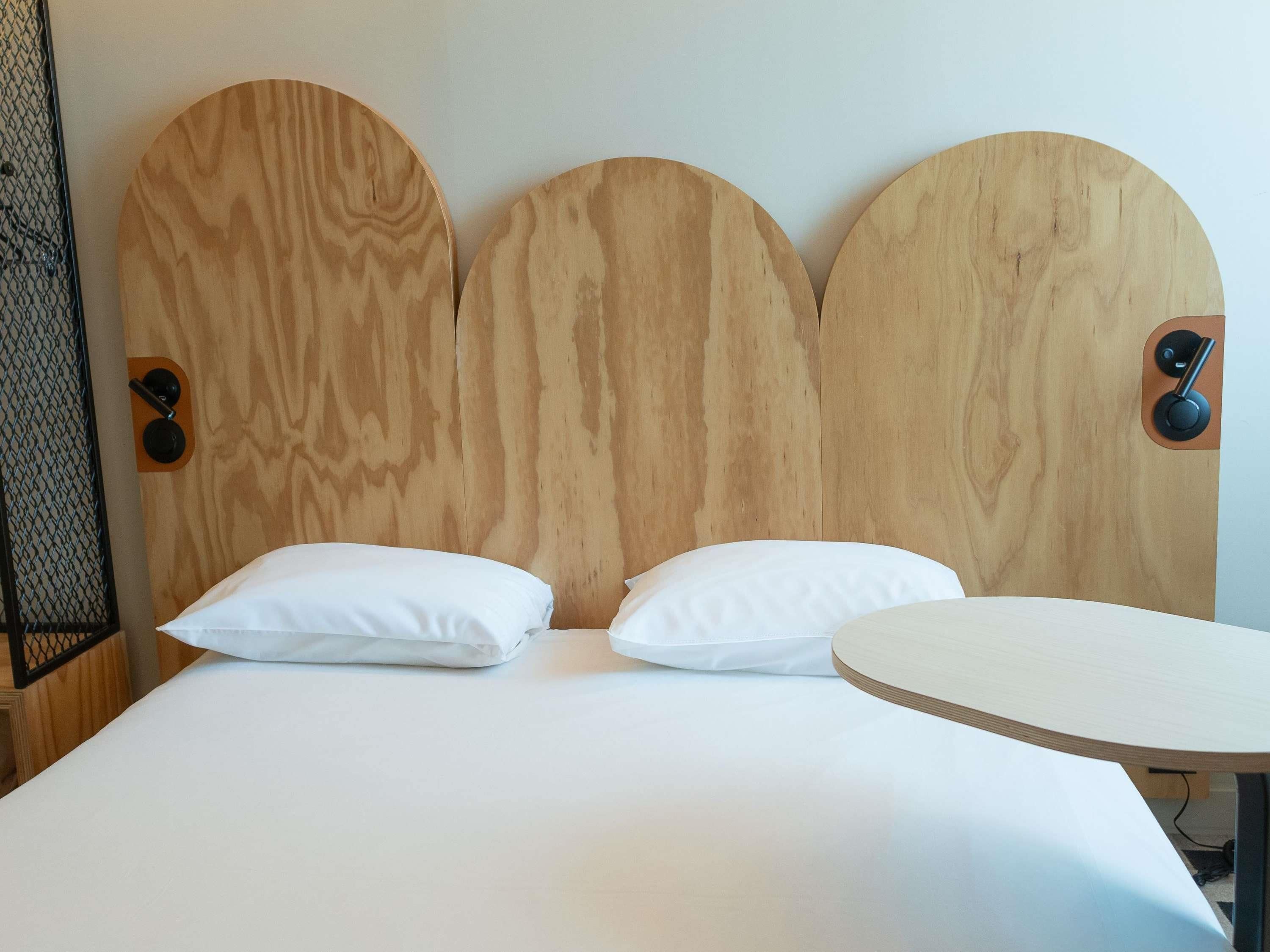 Ein Bett mit Holz-Kopfteil, zwei Kissen und einem runden Tisch.
