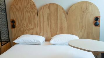 Ein Bett mit Holz-Kopfteil, zwei Kissen und einem runden Tisch.