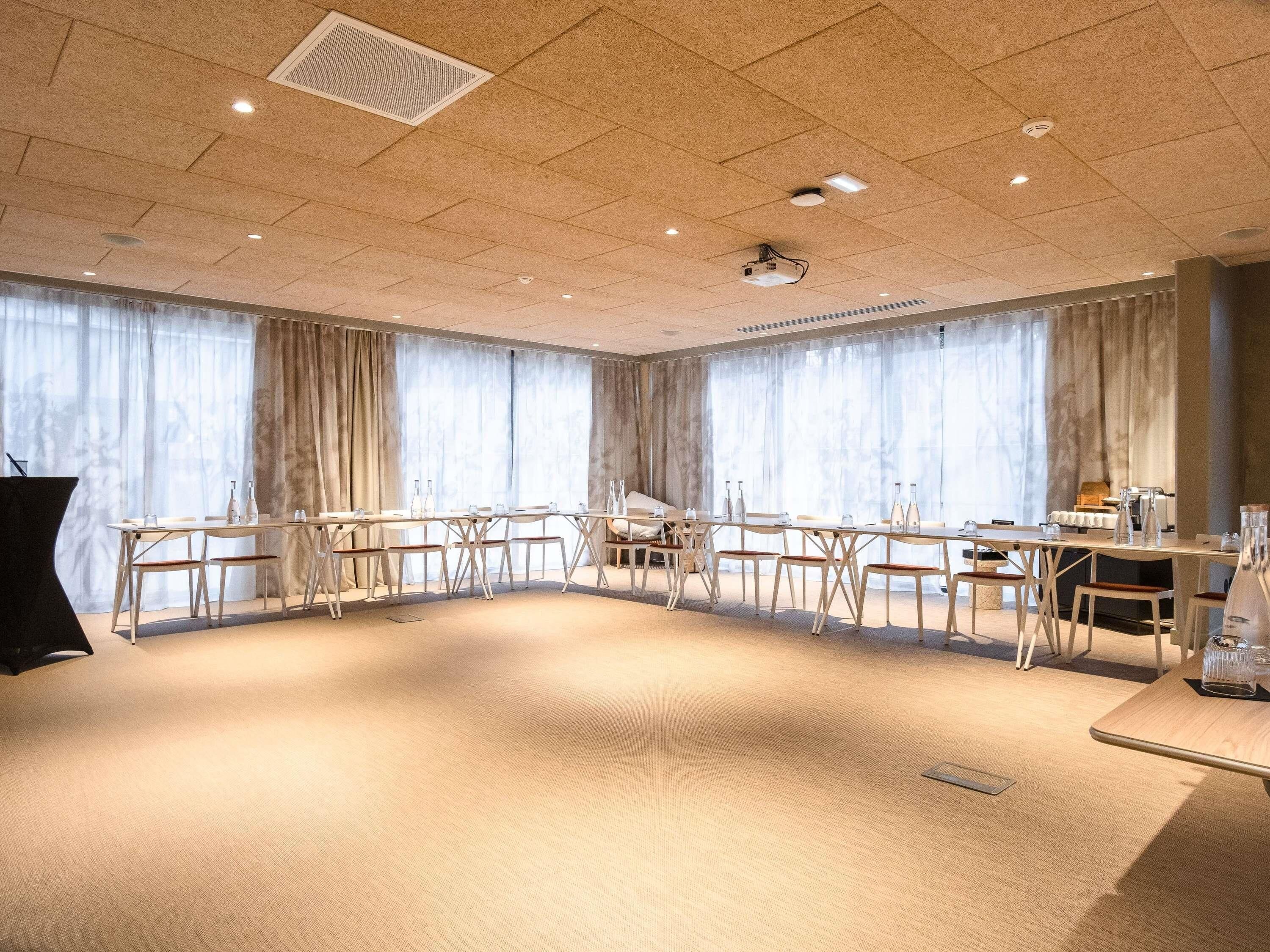 Una sala conferenze con un lungo tavolo, sedie, un proiettore e ampie finestre con tende.