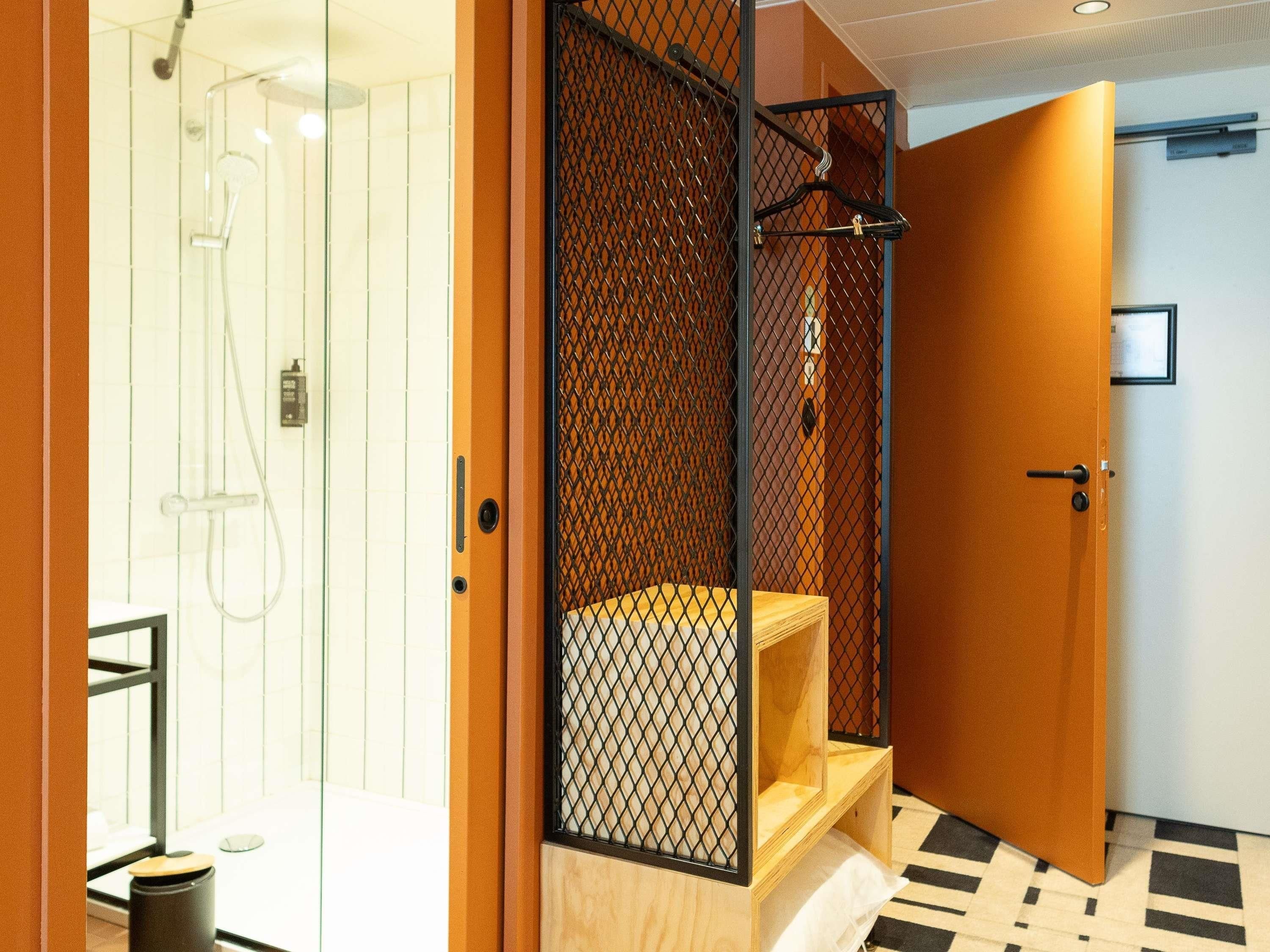 A hotel room with a shower, a wooden bench, and a door with a mesh screen.