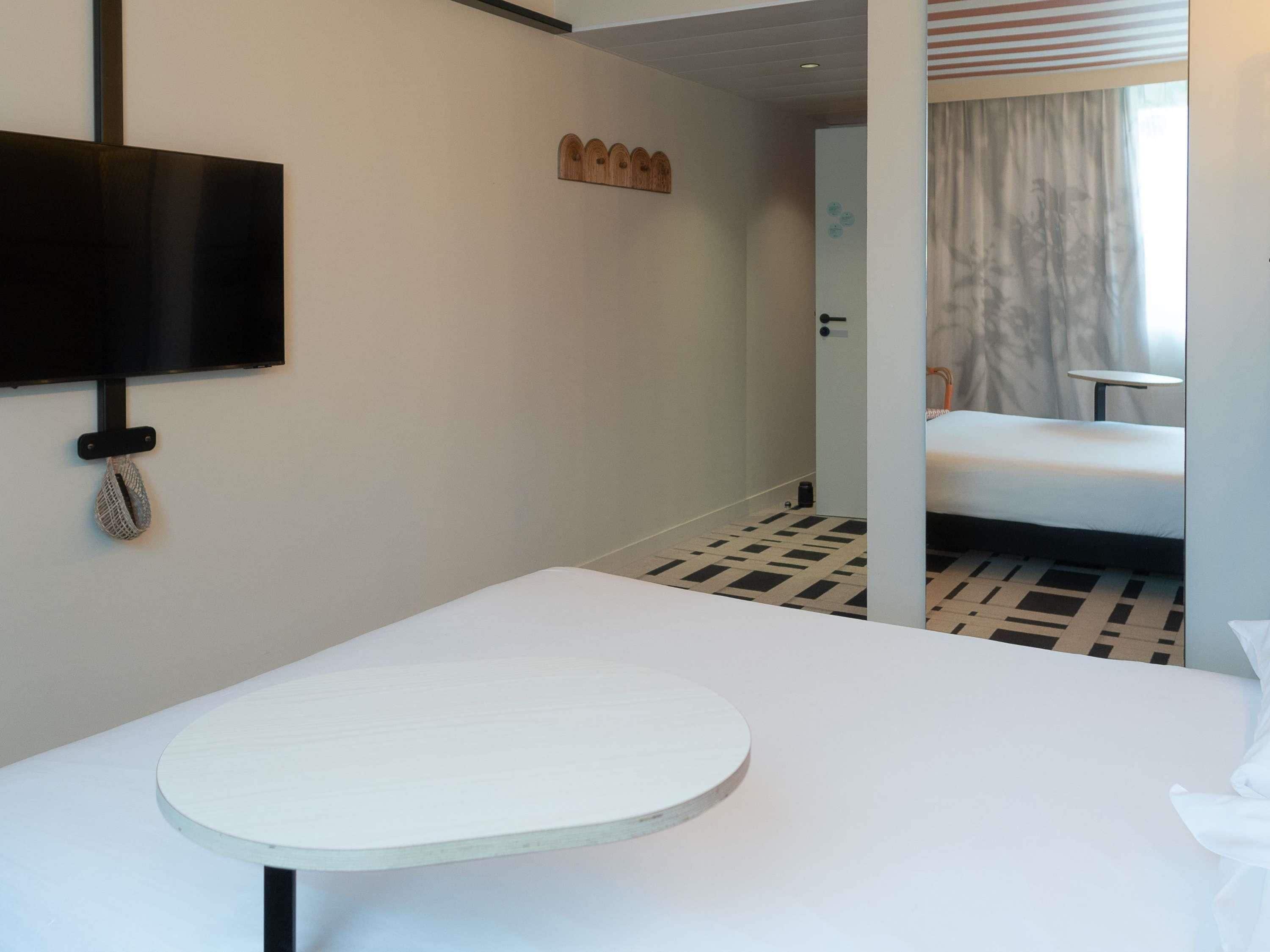 A hotel room with a bed, a round table, a TV mounted on the wall, and a patterned floor.