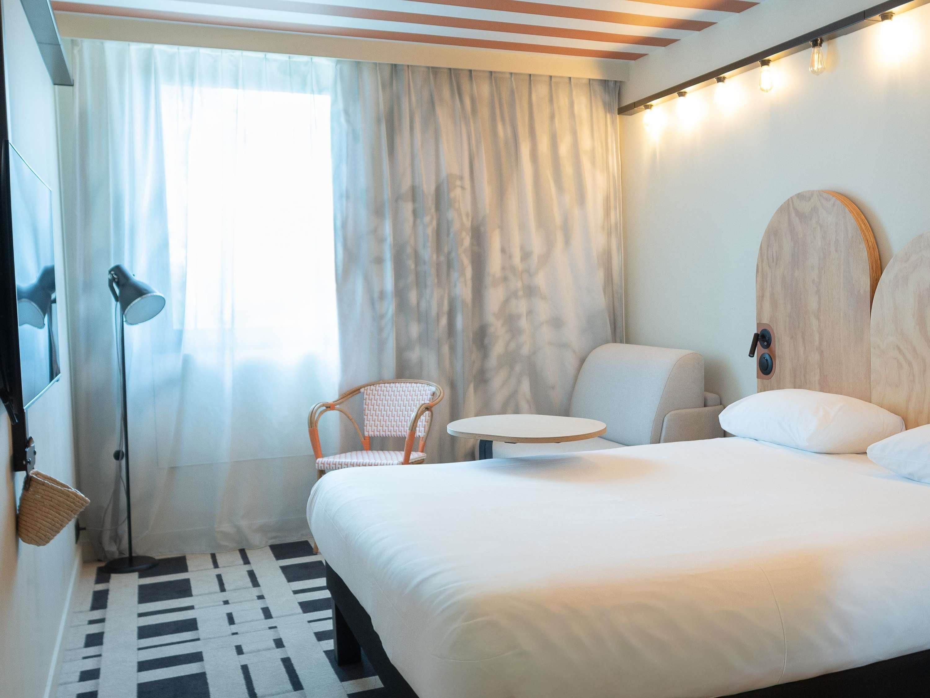 A hotel room with a bed, a chair, a small table, and a lamp.