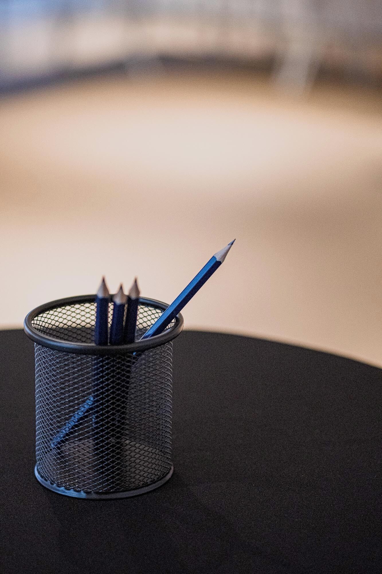 A mesh pencil holder with pencils on a dark surface.