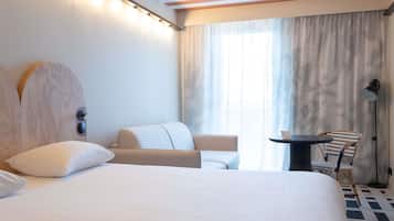 Una habitación de hotel con una cama, un escritorio, una silla y un amplio ventanal con cortinas.