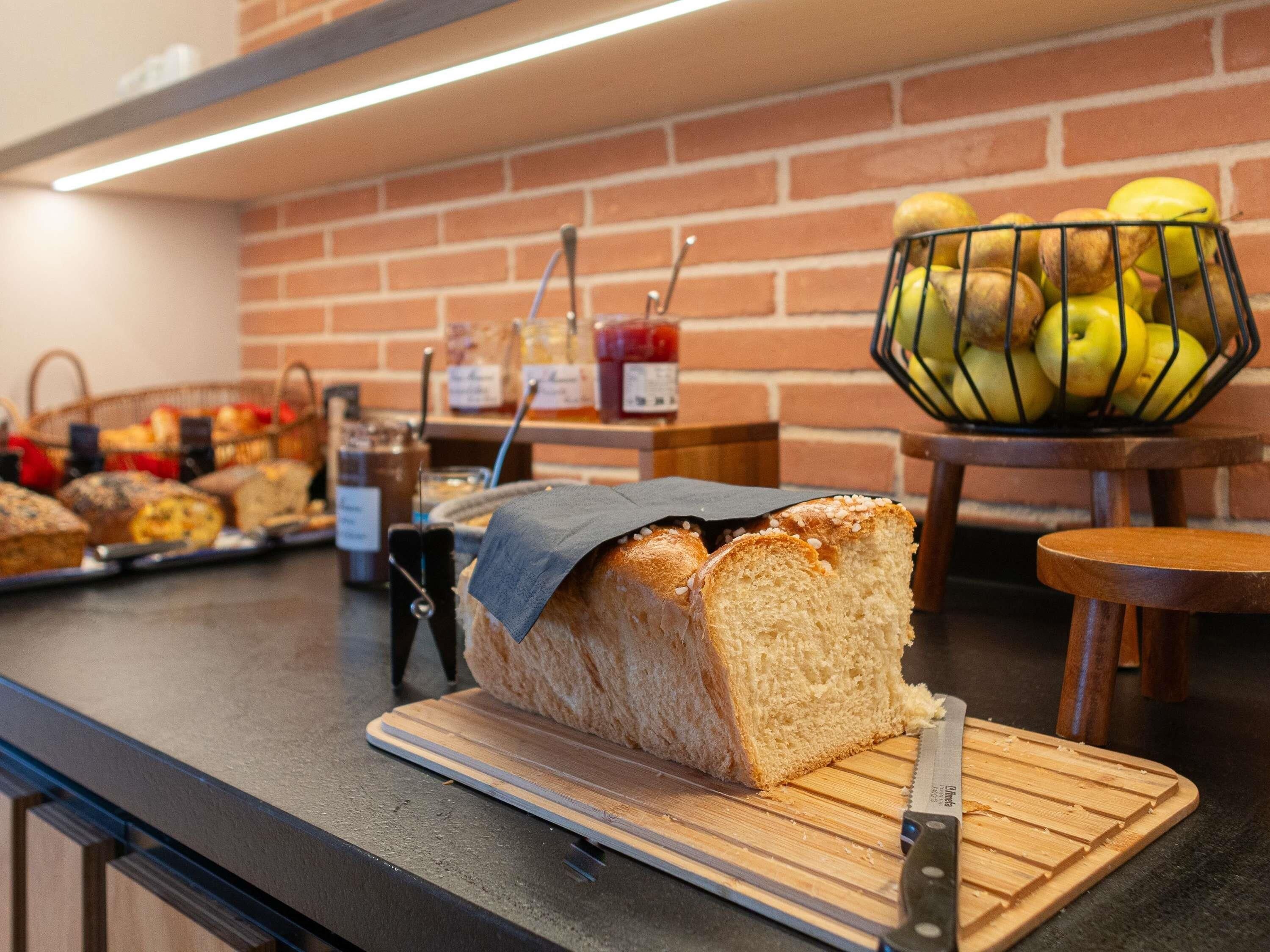 Vitrine de pastelaria com pão e doces, tábua de corte com faca e uma cesta de maçãs.